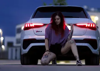 Nachtaufnahme einer Frau posierend vor den Rücklichtern ihres Autos