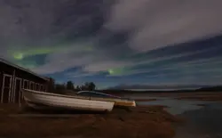 Boote im Mondlicht mit Nordlichtern hinter Wolken