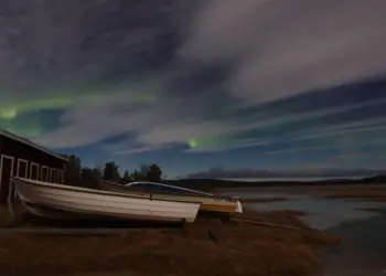 Boote im Mondlicht mit Nordlichtern hinter Wolken