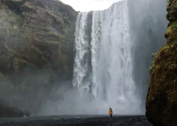 Frau im gelben Mantel vor dem Skogafoss auf Island