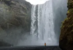 Frau im gelben Mantel vor dem Skogafoss auf Island