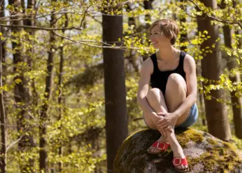 Ganzkörperaufnahme einer Frau im Wald sitzend auf einem Stein