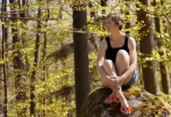 Ganzkörperaufnahme einer Frau im Wald sitzend auf einem Stein