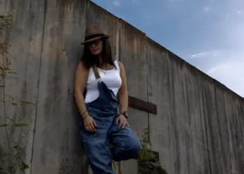 Ganzkörperaufnahme einer Frau in Latzhose an einer Betonwand