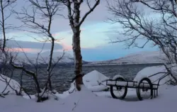 Handwagen am verschneiten Ufer eines Sees in der Abenddämmerung in Schweden