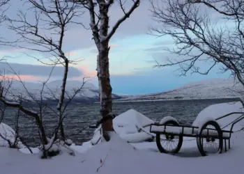 Handwagen am verschneiten Ufer eines Sees in der Abenddämmerung in Schweden