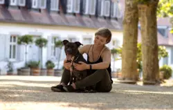Im Schatten der Allee sitzt eine Frau mit ihrem Hund