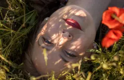 Frau liegend im Mohnfeld mit Blick in die Kamera